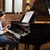 Child sat at grand piano using adsilent system app with headphones and a phone