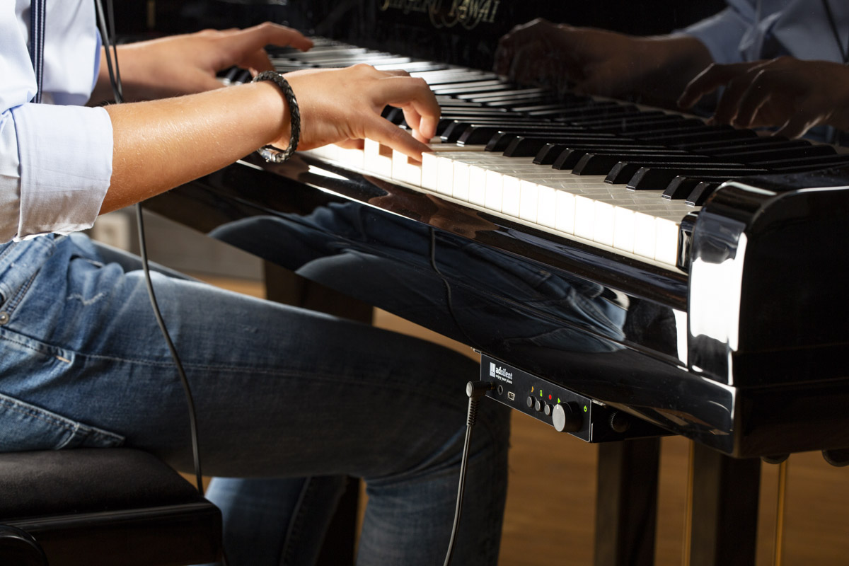 Adsilent system shown attached underneath acoustic piano keyboard with child playing the piano with headphones on